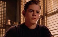 a young man sitting in front of a window with blinds on the windowsills