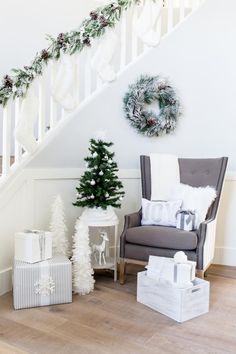 a christmas tree sitting next to a chair in front of a stair case with presents on it