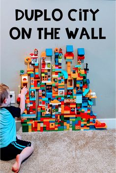 a young boy playing with a lego city on the wall that is made out of blocks