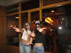 two women standing in front of a store window with their hands up and pointing at the camera