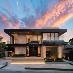 a modern house with stairs leading up to it's front door and windows at dusk