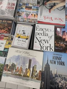 many books are stacked on top of each other in front of a wall covered with new york cityscapes