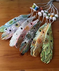 several different colored feathers hanging on a wooden table next to beads and beaded necklaces