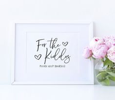 a vase filled with pink flowers sitting next to a white framed print that says for the kids