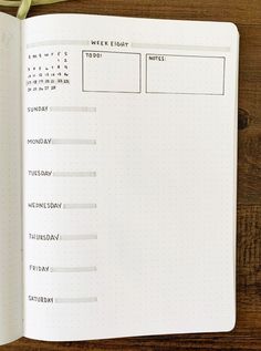 an open planner book on a wooden table with a pen and paper in front of it