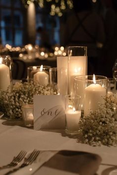 candles are lit in glass vases with flowers and greenery on the table, along with other place settings