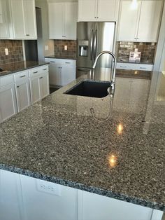 a kitchen with granite counter tops and white cabinets, an island style sink and stainless steel appliances