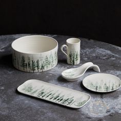 three ceramic dishes and two spoons with trees painted on them sitting on a table