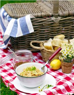 a bowl of noodles on a table with bread and lemons in the basket next to it