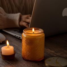 a candle sitting on top of a wooden table next to a laptop