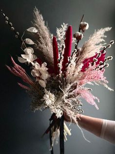 a vase filled with lots of red and white flowers next to a hand holding it