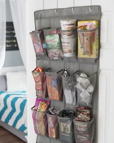 a wall hanging organizer filled with lots of snacks and candy bar items in front of a bed