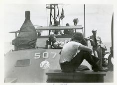 an old black and white photo of men sitting on a boat looking at something in the water