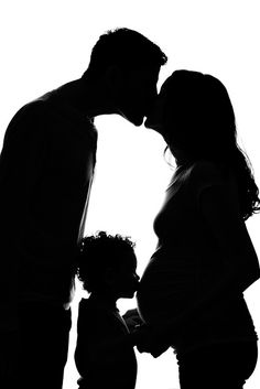 a man and woman kissing while standing next to a baby in front of a white background