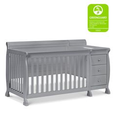 a gray crib with drawers and white sheets on the bottom, in front of a greenguard sticker