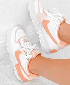 a woman's legs wearing white and orange nike air force sneakers with her feet propped up against the wall