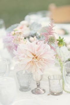 an arrangement of flowers in vases on top of a table with glasses and napkins