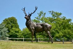 a statue of a stag stands in the middle of a grassy field with trees behind it