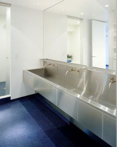 an empty public bathroom with blue carpeting and stainless steel sinks on the wall,