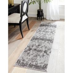 a white and gray area rug in a living room with a black chair, potted plant and window