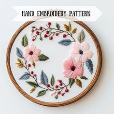 a hand embroidery pattern with pink flowers and leaves on it, in a wooden hoop