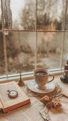 a cup of coffee sitting on top of a table next to an open book and pocket watch