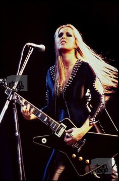 a woman with long hair holding a guitar in front of a microphone