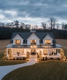 a large white house with christmas lights on it's front porch and trees in the yard