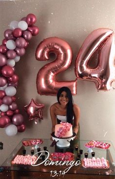 a woman sitting at a table with a cake and balloons in the shape of numbers