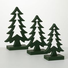 three small green christmas trees are standing in front of each other on a white surface