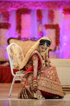 a woman in a red and gold wedding dress sitting on the floor with her feet up