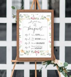 a sign that is on top of a easel with flowers and greenery around it