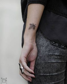 a woman's arm with a small leaf tattoo on the left side of her wrist