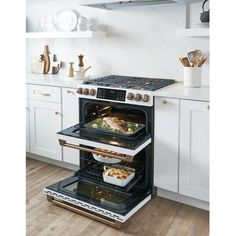 two open ovens in a kitchen with white cabinets and wood flooring, one has food on the bottom shelf