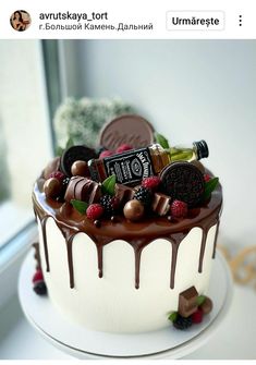 a white cake with chocolate icing and assorted candies on top, sitting in front of a window