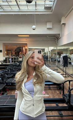 a woman taking a selfie with her cell phone in a gym room filled with exercise equipment