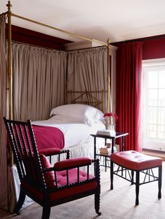 a bedroom with a canopy bed and red drapes on the windowsill, two chairs in front of it