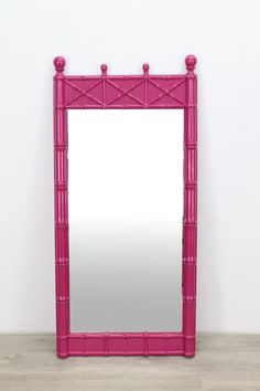 a large pink mirror sitting on top of a wooden floor next to a white wall