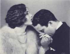 an old black and white photo of a man kissing a woman's face with pearls on her necklace