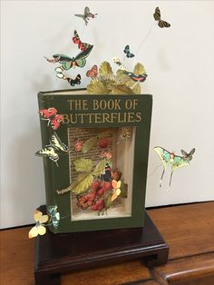 the book of butterflies is on top of a wooden stand with several butterflies flying around it