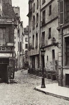 an old black and white photo of a cobblestone street with buildings in the background