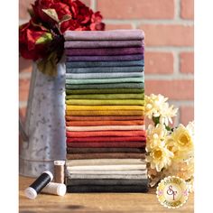 a stack of towels sitting on top of a wooden table next to a vase filled with flowers