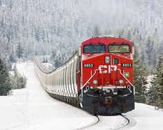 a red train traveling down tracks next to snow covered trees and evergreens in the background