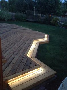 a wooden deck with lights on it and grass in the back yard area behind it