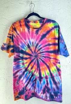 a colorful tie - dyed shirt hanging on a white wall with a black hanger