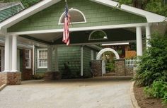 a green house with an american flag hanging from it's front door and porch