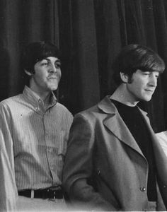 three men are standing next to each other in front of a curtained window, one is wearing a suit and the other wears a tie