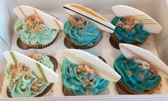 six cupcakes in a box with surfboards and sand on the top one