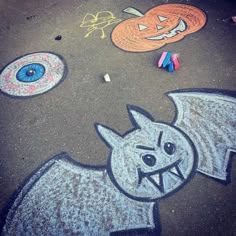 some chalk drawings are on the ground and one has a bat, pumpkins, and two eyes