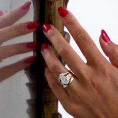 a woman's hand with red nail polish holding a gold and diamond ring on her finger